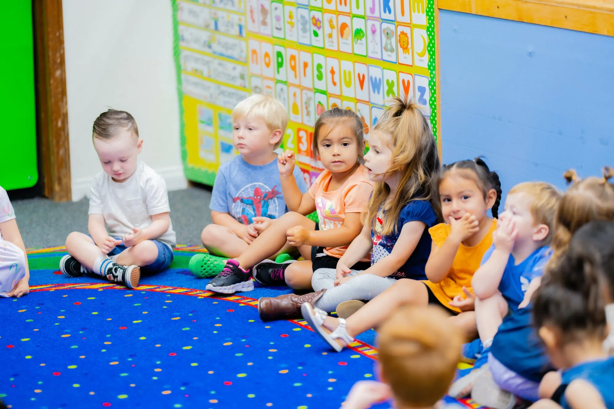 Preschool children sit together on a blue rug during circle time.