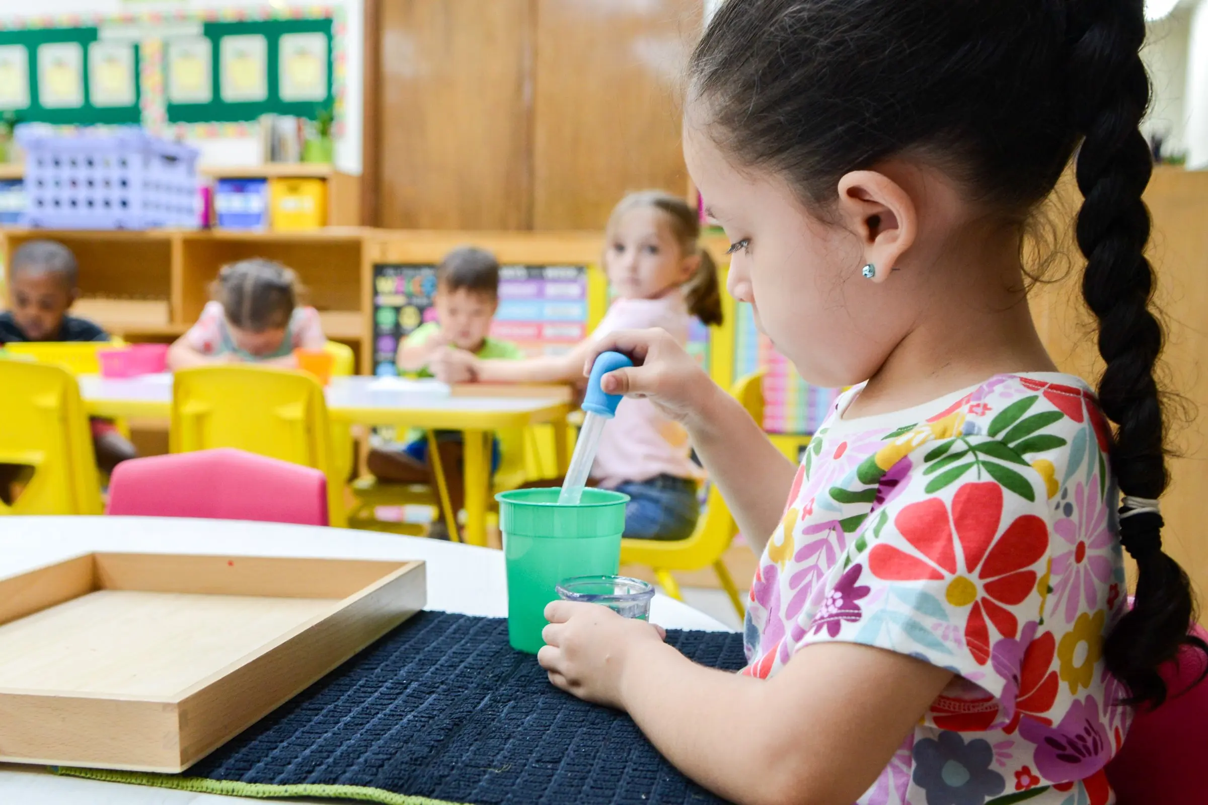 A girl carefully uses a dropper to move water between glasses.