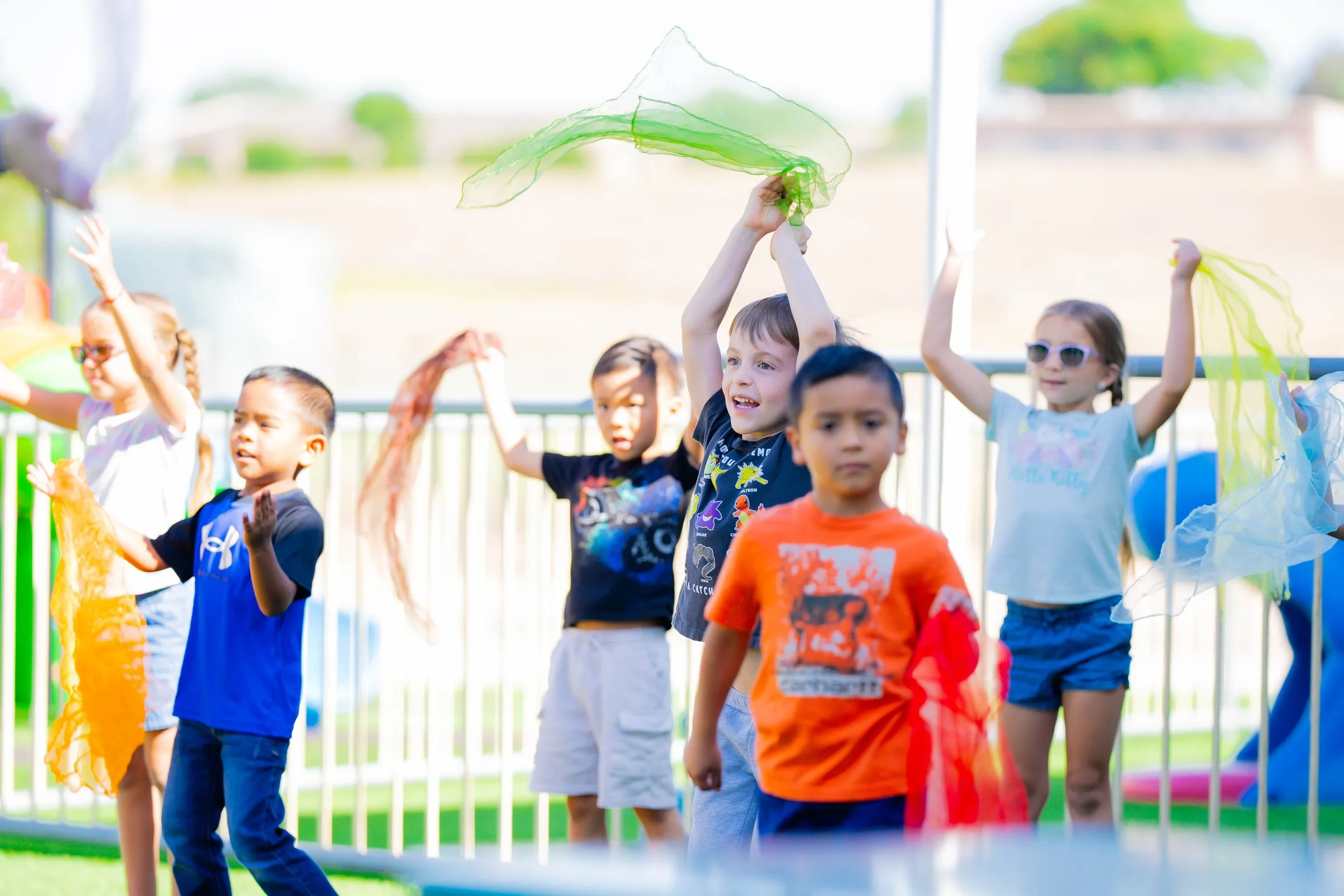 Children dance outdoors waving colorful scarves above their heads.